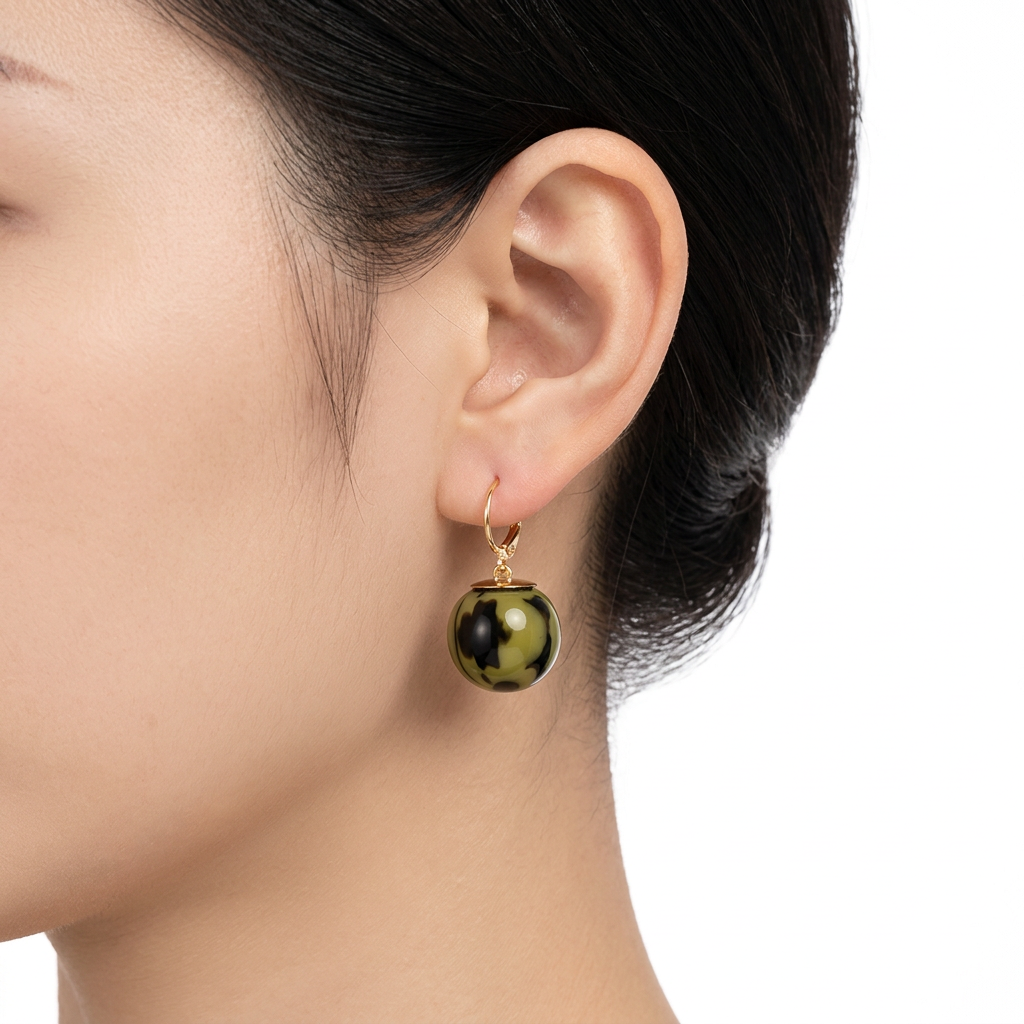 Kolczyk ze złotym zapięciem i zielono-czarną kulką na modelce na białym tle
